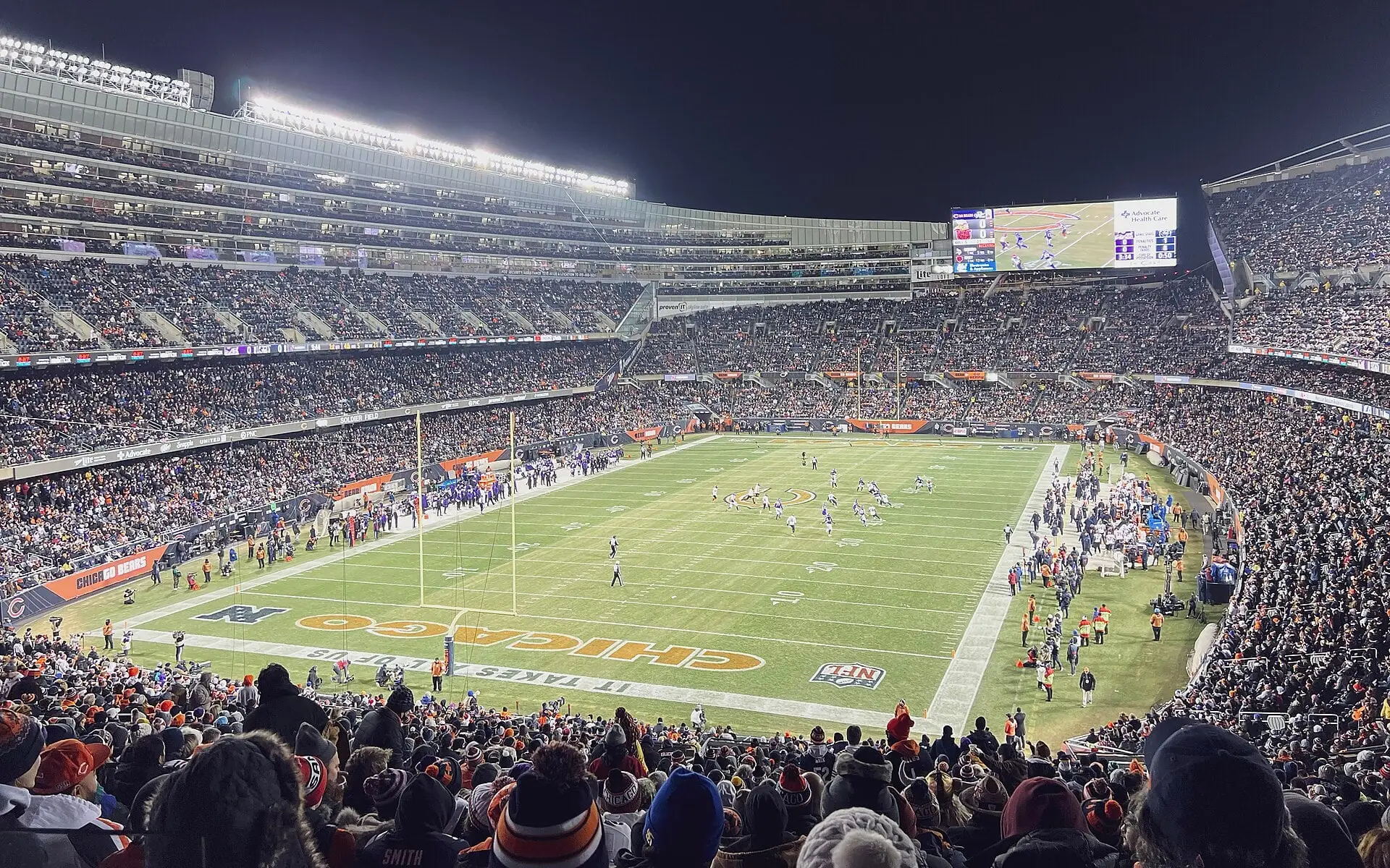 Soldier Field seating bowl and field from the upper deck at night during a Bears home game, with the video board and the modern stands wrapping the playing surface