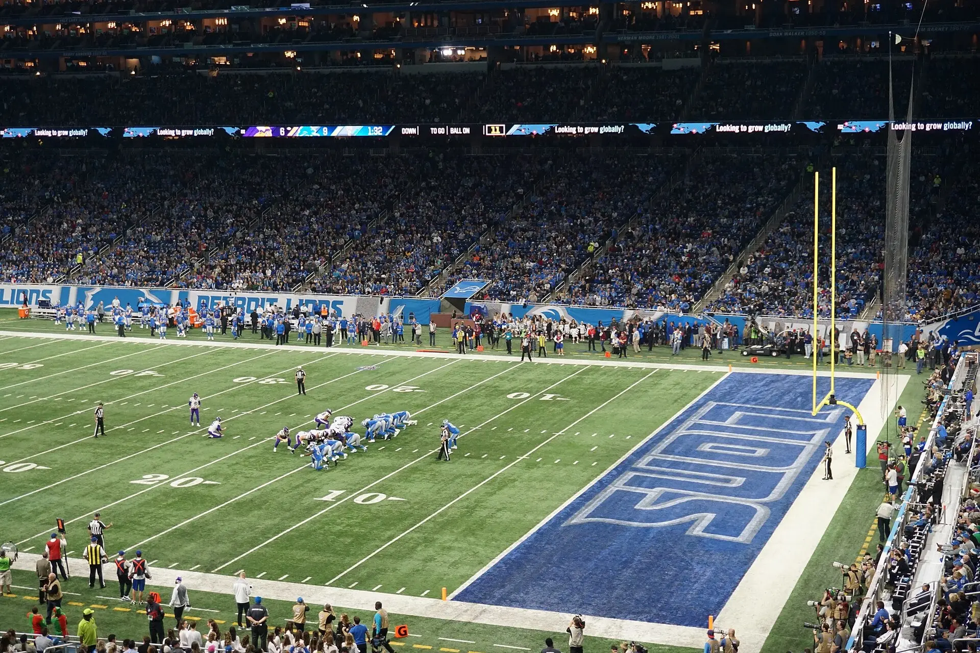 Elevated view across the field at Ford Field during a Lions game, with the upper and lower seating decks and the blue end zone visible