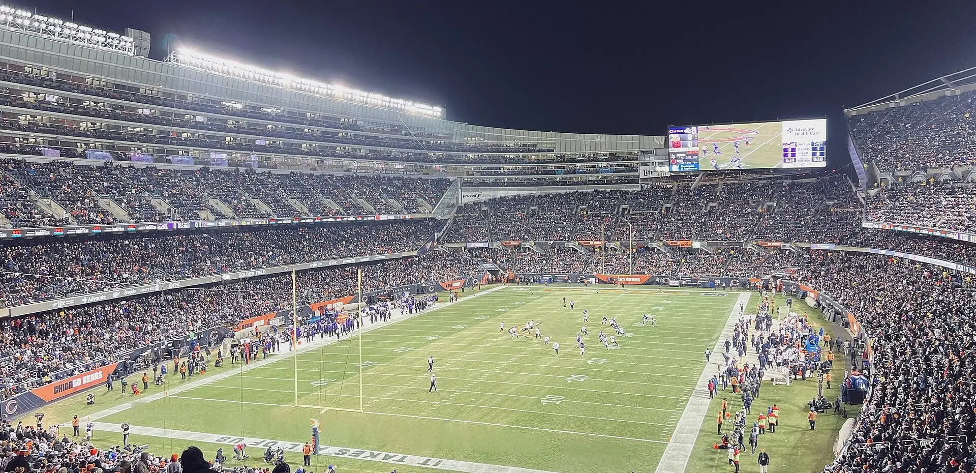 Soldier Field seating bowl and field from the upper deck at night during a Bears home game, with the video board and the modern stands wrapping the playing surface