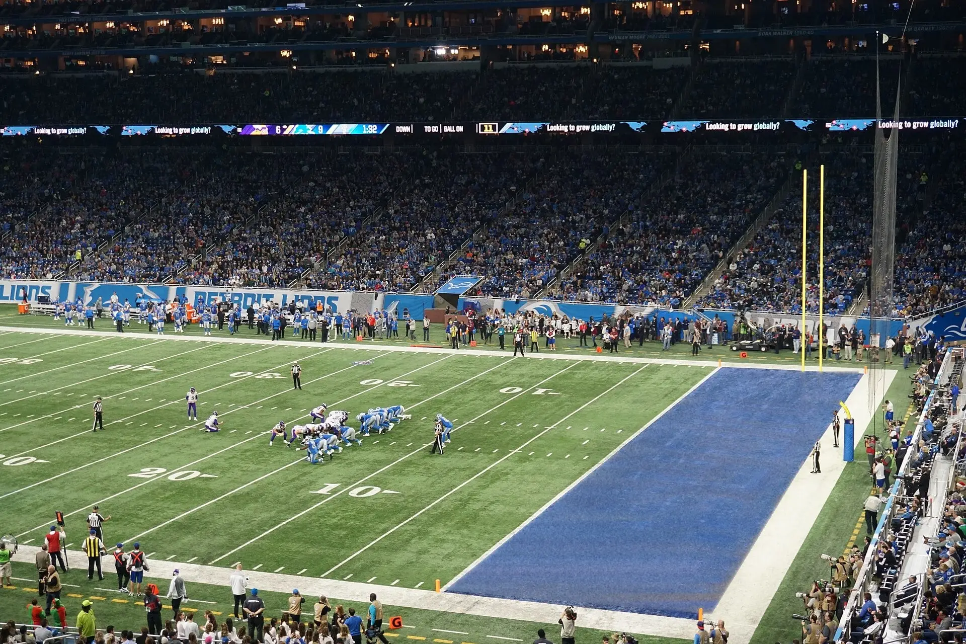 Elevated view across the field at Ford Field during a Lions game, with the upper and lower seating decks and the blue end zone visible